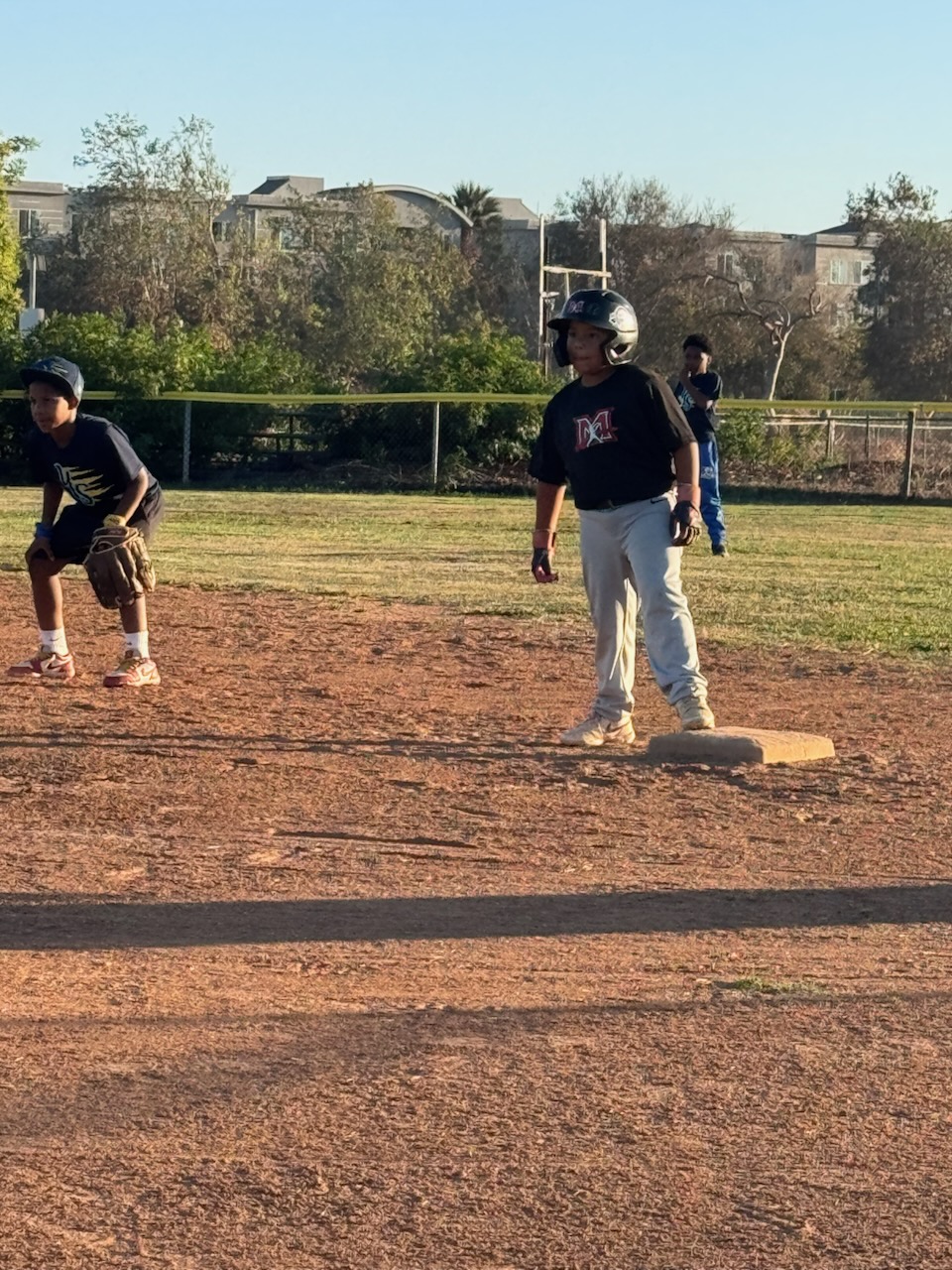 Two 9U players in black Martinez jerseys — one standing on a base, one crouched ready — during a practice on a dirt infield